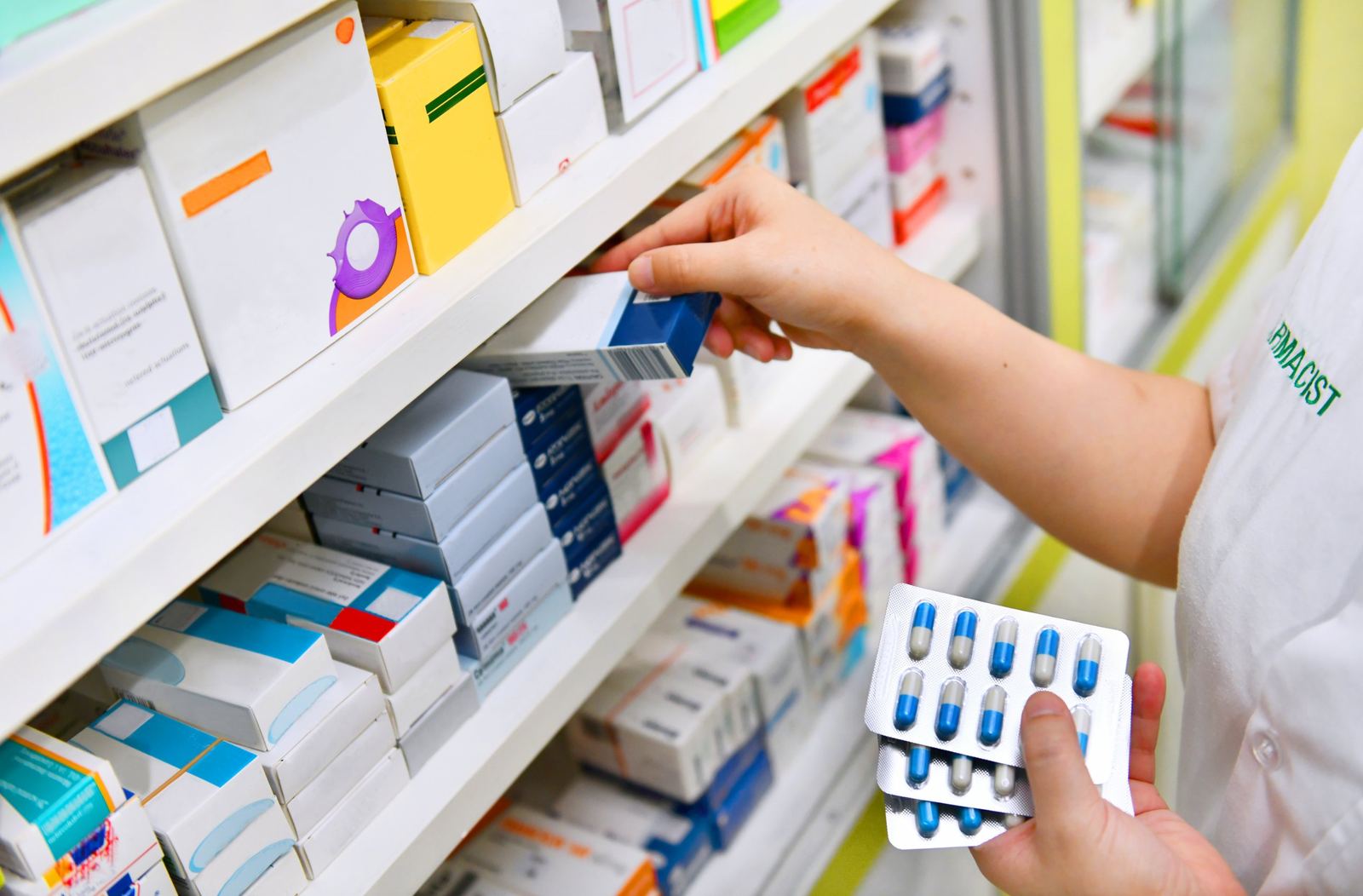Farmacéutica tomando una caja de medicamento de la estantería